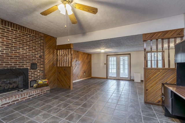 unfurnished living room with a textured ceiling, dark tile patterned flooring, wood walls, a fireplace, and french doors