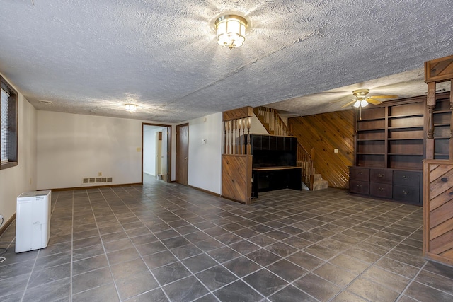 unfurnished living room featuring dark tile patterned floors, wooden walls, visible vents, and a textured ceiling