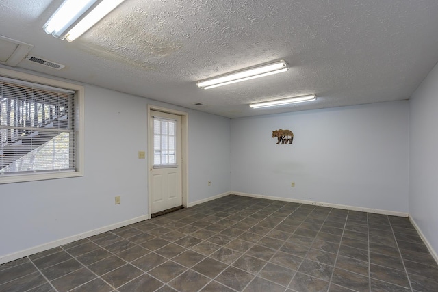 spare room featuring a textured ceiling, visible vents, and baseboards