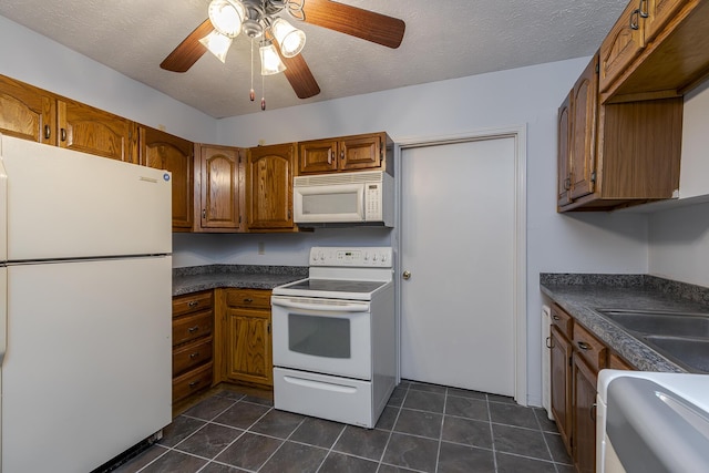 kitchen featuring dark countertops, white appliances, brown cabinets, and dark tile patterned flooring