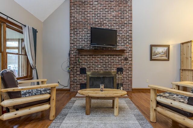 living room featuring lofted ceiling, a brick fireplace, wood finished floors, and baseboards