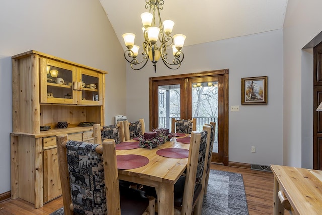 dining room with light wood finished floors, baseboards, visible vents, lofted ceiling, and a notable chandelier