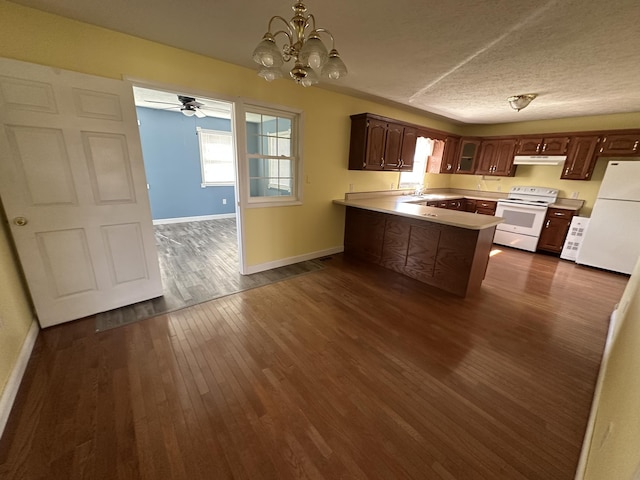 kitchen featuring a peninsula, white appliances, dark wood-style flooring, light countertops, and glass insert cabinets