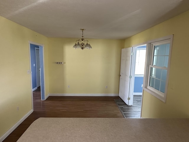 unfurnished dining area with a chandelier, baseboards, and dark wood-style floors