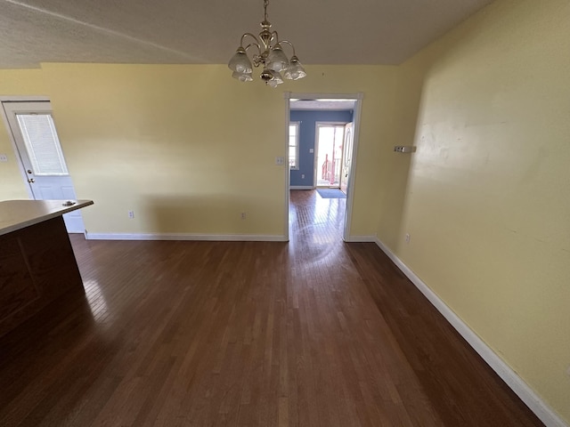 unfurnished dining area featuring dark wood-style floors, baseboards, and a chandelier