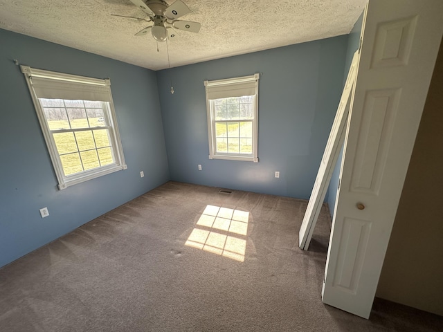 empty room with a textured ceiling, ceiling fan, carpet flooring, and visible vents