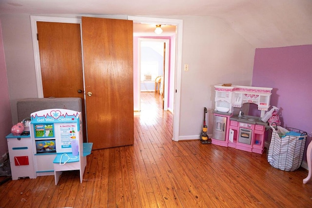 recreation room featuring vaulted ceiling, hardwood / wood-style flooring, and baseboards