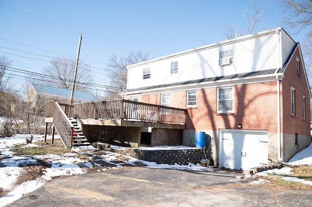 snow covered back of property with a wooden deck, stairs, and brick siding