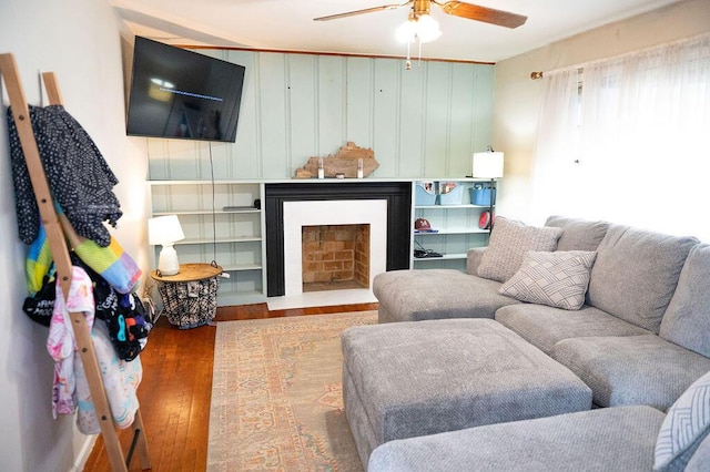 living area featuring a fireplace with flush hearth, a ceiling fan, and wood finished floors