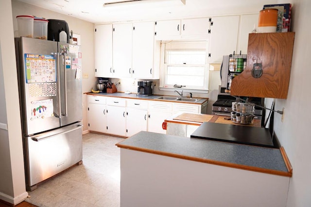 kitchen featuring light floors, freestanding refrigerator, white cabinets, a sink, and a peninsula