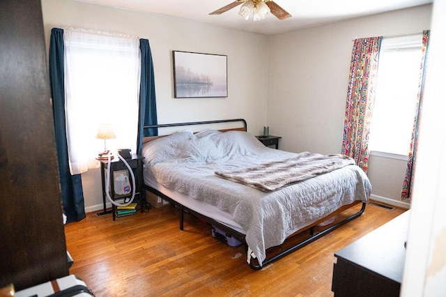 bedroom with a ceiling fan, visible vents, baseboards, and wood finished floors