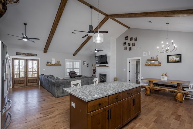 kitchen with visible vents, light wood-type flooring, a fireplace, ceiling fan with notable chandelier, and stainless steel fridge