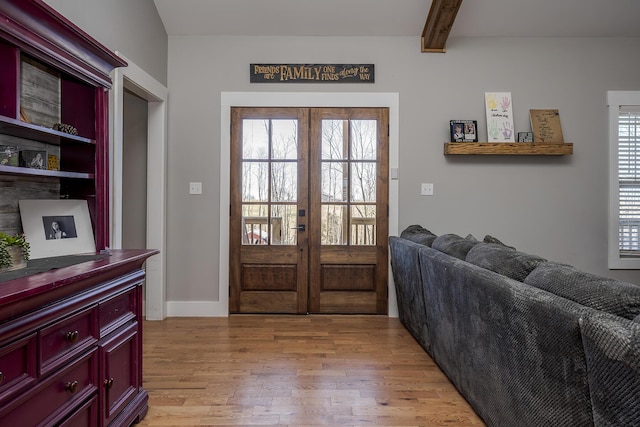 foyer entrance featuring french doors, beam ceiling, and light wood-style flooring