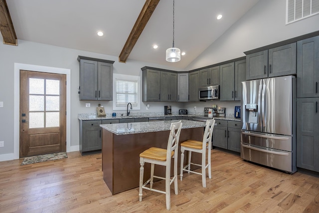 kitchen featuring visible vents, a sink, light stone counters, a kitchen island, and appliances with stainless steel finishes