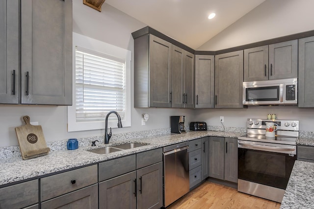kitchen featuring light wood-style flooring, a sink, light stone counters, appliances with stainless steel finishes, and lofted ceiling