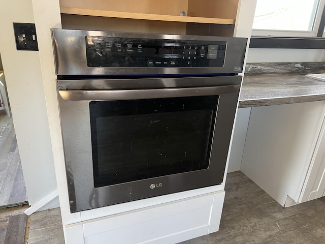 room details featuring wood finished floors, stainless steel oven, and white cabinetry