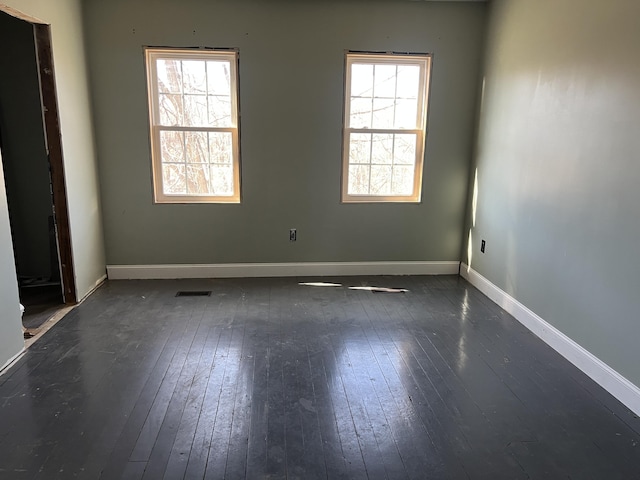 empty room featuring dark wood-style flooring, a wealth of natural light, and baseboards