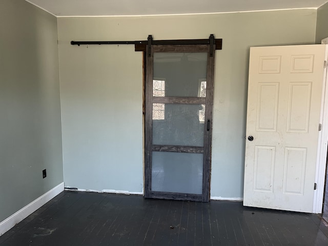 spare room with a barn door, dark wood-style flooring, and baseboards