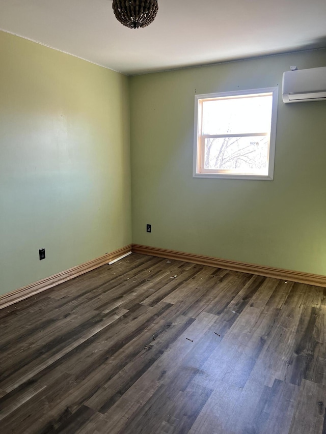 unfurnished room with dark wood-style flooring, a wall unit AC, and baseboards