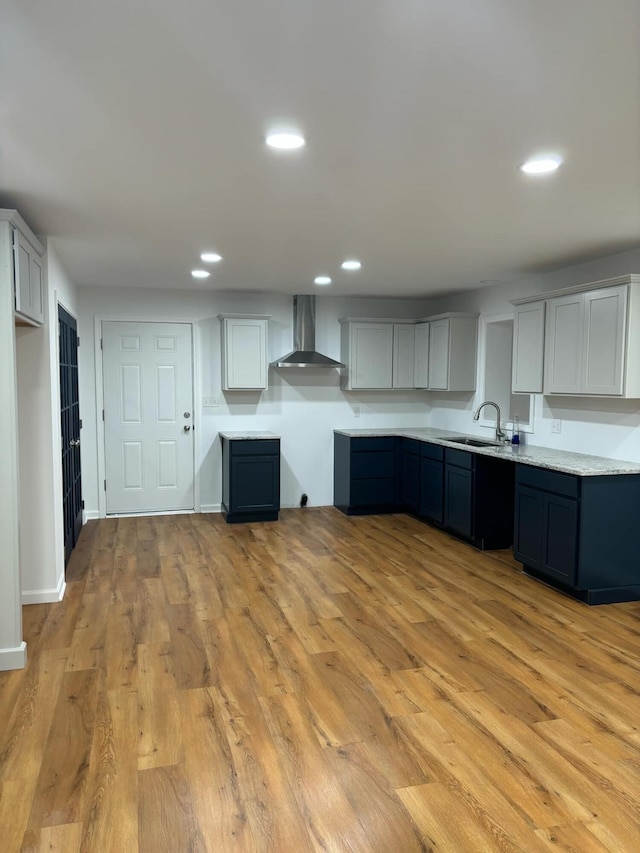 kitchen featuring recessed lighting, a sink, light countertops, light wood-type flooring, and wall chimney exhaust hood