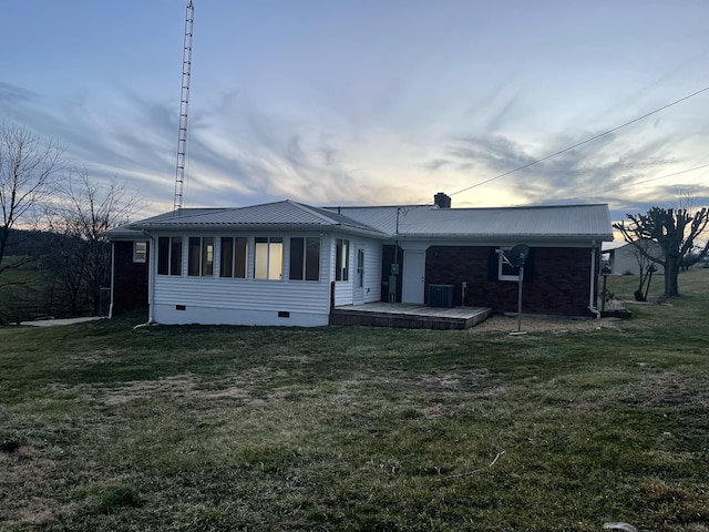 back of house at dusk featuring crawl space, a lawn, and metal roof