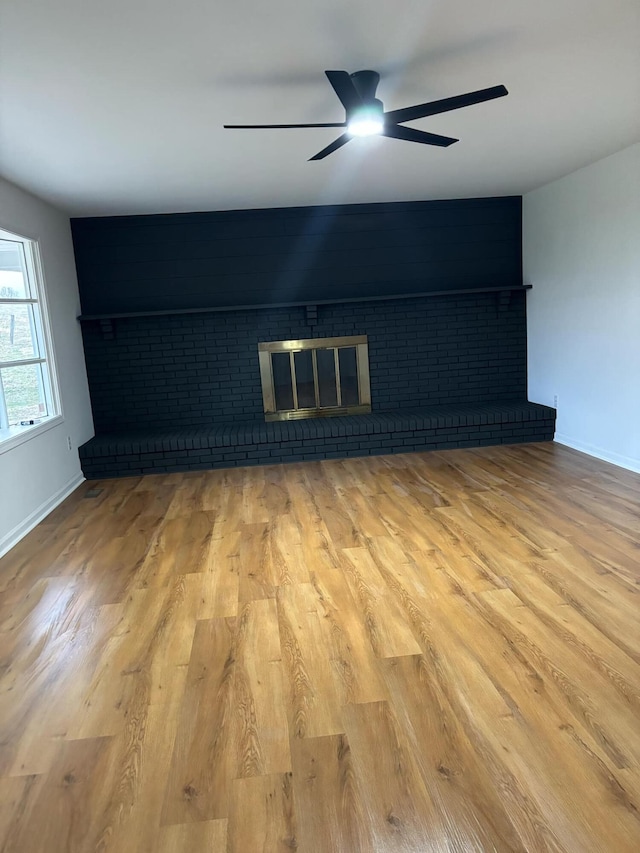 unfurnished living room featuring a brick fireplace, a ceiling fan, baseboards, and wood finished floors