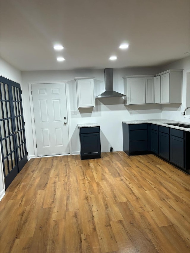 kitchen featuring recessed lighting, light countertops, light wood-style flooring, a sink, and wall chimney range hood