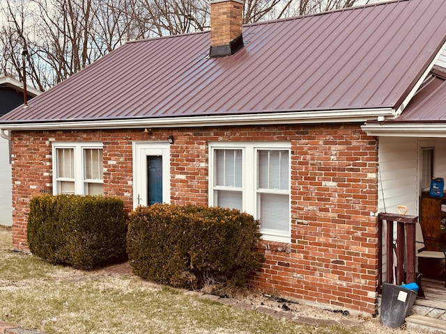 view of side of home with a standing seam roof, brick siding, metal roof, and a chimney