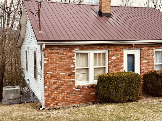 view of property exterior featuring brick siding, a chimney, a standing seam roof, central AC, and metal roof