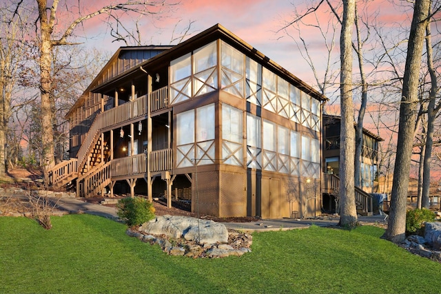 back of property at dusk featuring stairway, a lawn, and board and batten siding