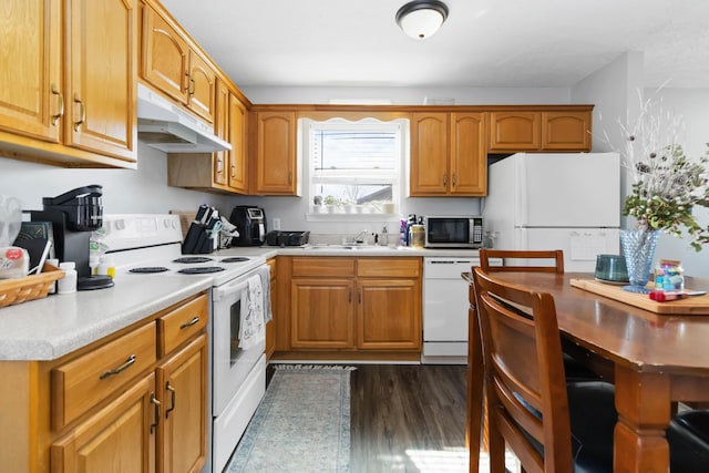 kitchen with under cabinet range hood, dark wood finished floors, light countertops, white appliances, and a sink