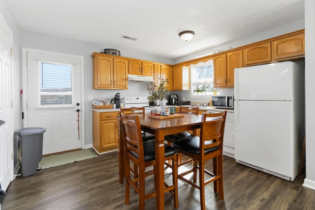 kitchen featuring visible vents, under cabinet range hood, dark wood finished floors, white appliances, and light countertops