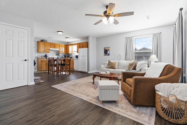 living room with visible vents, a textured ceiling, dark wood-style floors, baseboards, and ceiling fan