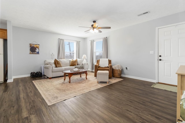 living area with dark wood-style floors, visible vents, a ceiling fan, and baseboards