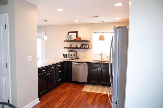 kitchen featuring light stone counters, a sink, appliances with stainless steel finishes, backsplash, and dark wood-style floors