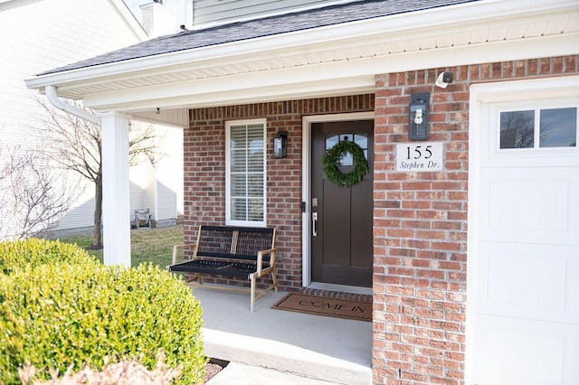 doorway to property featuring a garage, brick siding, roof with shingles, and covered porch