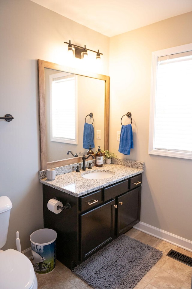 half bath featuring baseboards, vanity, toilet, and a healthy amount of sunlight