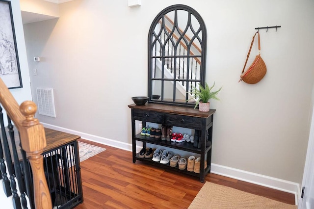 hallway with stairway, wood finished floors, visible vents, and baseboards