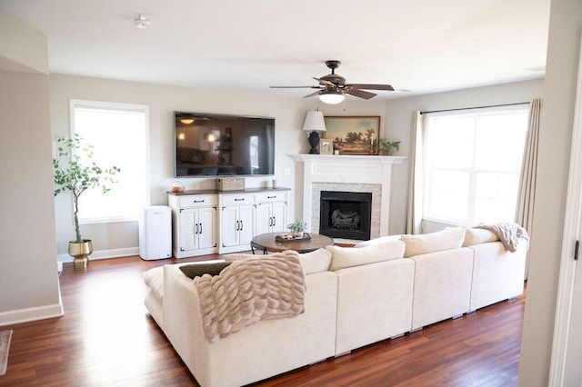 living area featuring a fireplace, dark wood finished floors, baseboards, and ceiling fan