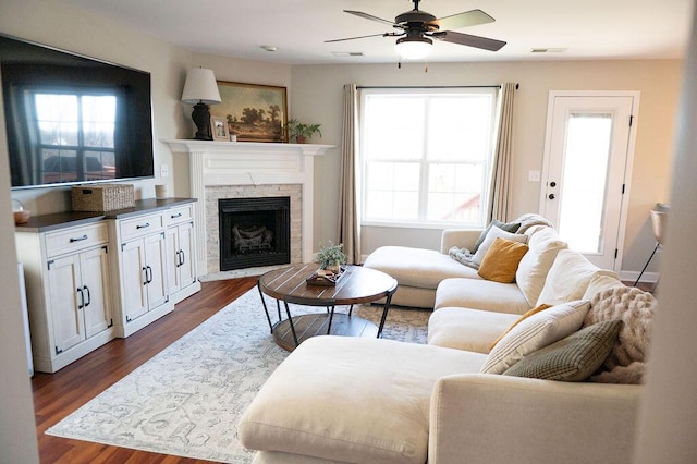 living room featuring dark wood-style flooring, a fireplace, visible vents, and a ceiling fan