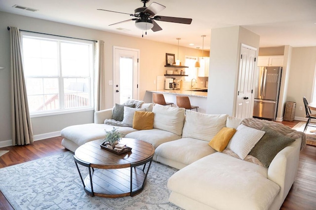 living area featuring a ceiling fan, baseboards, visible vents, and wood finished floors