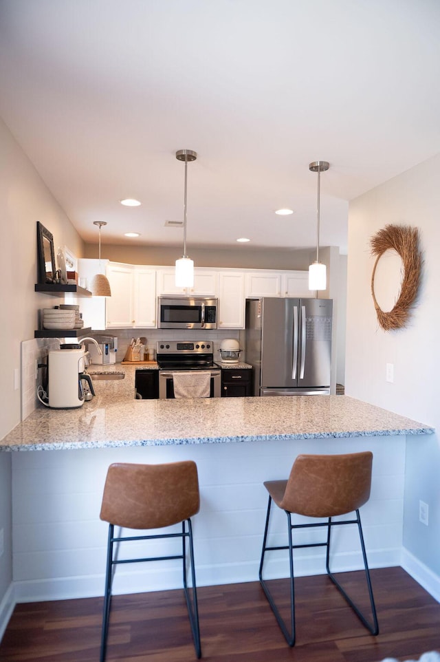 kitchen with a peninsula, light stone countertops, appliances with stainless steel finishes, and dark wood-type flooring