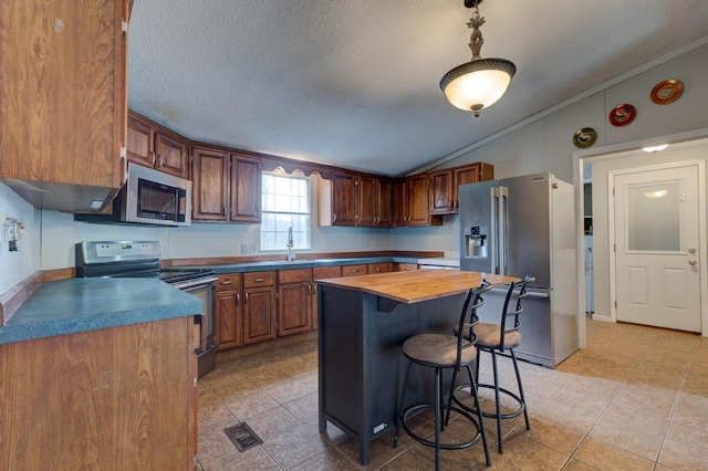 kitchen with lofted ceiling, a textured ceiling, stainless steel appliances, a kitchen island, and a sink