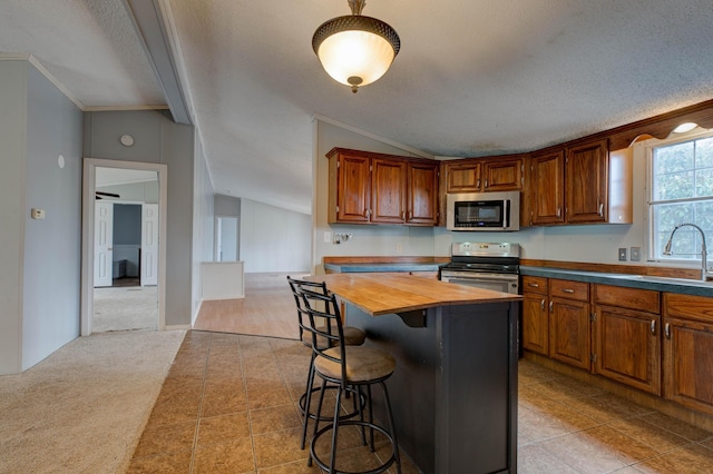 kitchen with light colored carpet, stainless steel appliances, a breakfast bar, wood counters, and vaulted ceiling