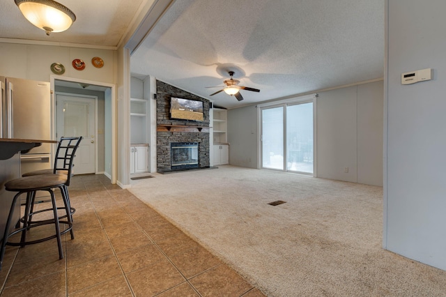 tiled living room featuring built in features, lofted ceiling, carpet flooring, a stone fireplace, and a textured ceiling