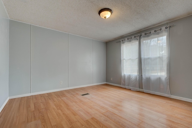 empty room featuring baseboards, a textured ceiling, visible vents, and wood finished floors