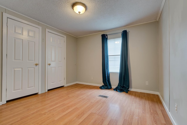 empty room with visible vents, light wood-style flooring, and a textured ceiling