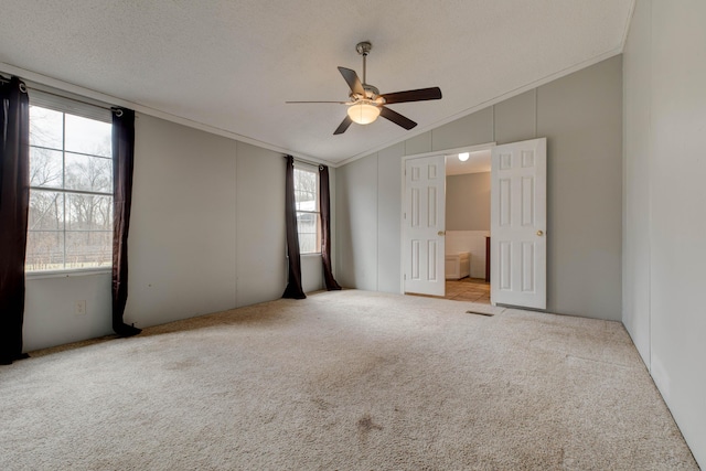 spare room with crown molding, a ceiling fan, carpet flooring, vaulted ceiling, and a textured ceiling