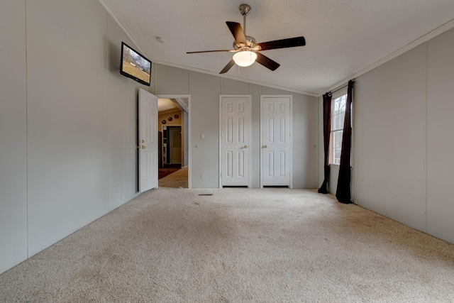 unfurnished bedroom featuring crown molding, carpet flooring, vaulted ceiling, and two closets