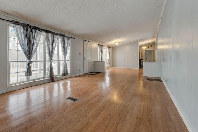 unfurnished living room with visible vents, vaulted ceiling, a textured ceiling, light wood-type flooring, and baseboards